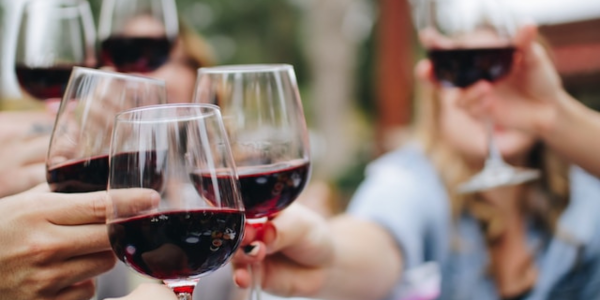 A photo of a glass of red wine with friends and vineyard in the background.